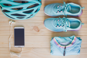 Top view of sport equipment in pastel colour: helmet, shoes, biking clothes, biking gloves, socks, smart phone, earplug, and notebook on wooden background