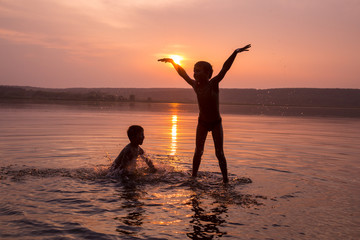 Two boys jumping into water on sunset