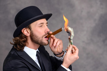 businessman with bowler hat lighting big cigar with money