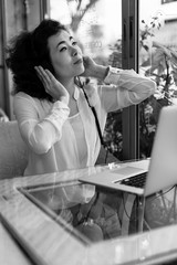 Asian girl sitting at a table in a cafe with a laptop, in headphones to enjoy music. Black and white photo.