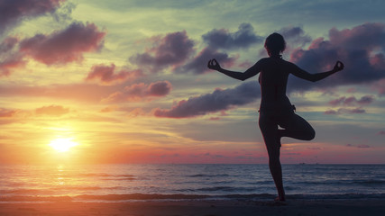 Fototapeta na wymiar Yoga woman exercising on the beach during a stunning sunset. Peace, harmony, health and meditation.