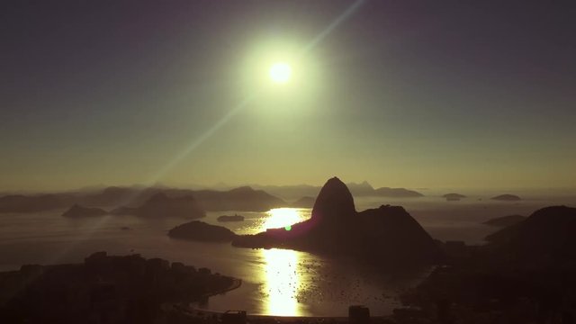 An airplane flies across scenic sunrise view over Sugarloaf Mountain and Guanabara Bay from an overlook in Rio de Janeiro, Brazil