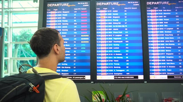 Male traveler backpacker looking at airport schedule screen