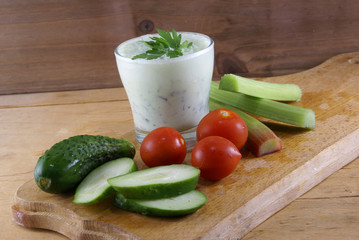 Useful summer snack: vegetables and yogurt sauce with herbs. Against the background of a rustic wooden table