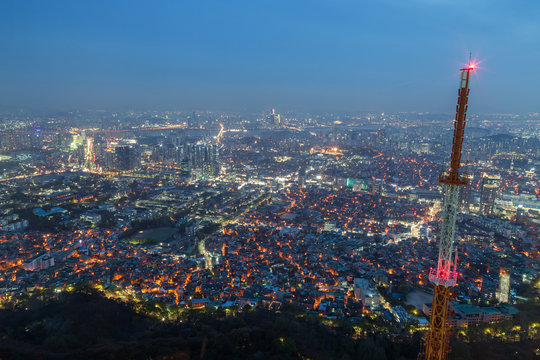 View of skyline in Seoul, South Korea, from above at night. A tall radio tower is on the foreground.