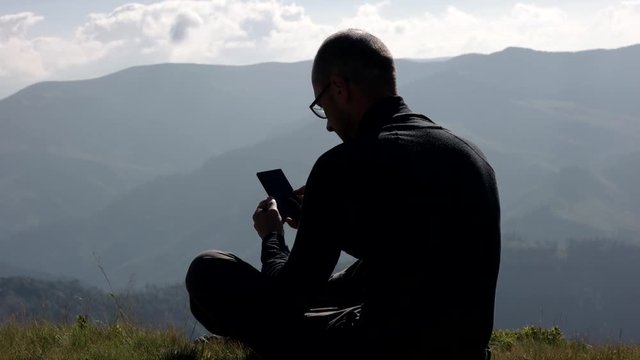 Young Man Using a Mobile Phone on a Mountain Top With Landscape Background