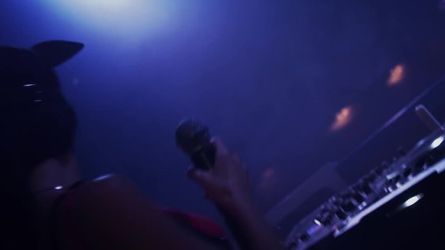 Back side of mc girl and Dj girl in masks dance at turntable in nightclub. Party. Spotlights