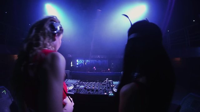 Back side mc girl and dj girl in hare mask at turntable in nightclub. Dance. Blue spotlights.