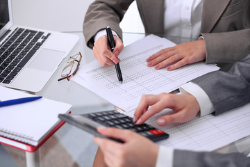 Two female accountants counting on calculator income for tax form completion hands closeup....