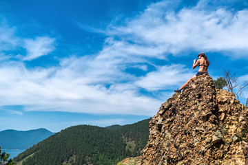 girl in swimsuit sits on a cliff-top Skriper