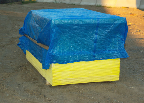 wooden stacked plywood or gyproc panels covered with a tarp on construction site
