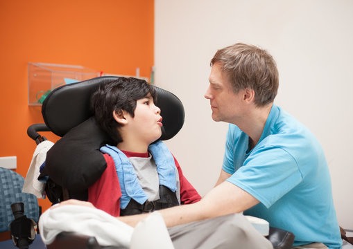 Disabled little boy in wheelchair talking with father in hospita