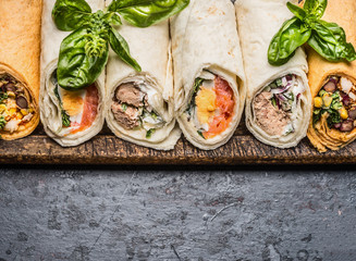 Various of tasty tortilla wraps on dark rustic background, top view, border. Healthy street food