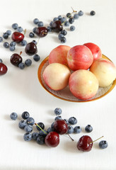 Berry mix. Peaches in a bowl, cherry and bilberry. A white cloth from flax.