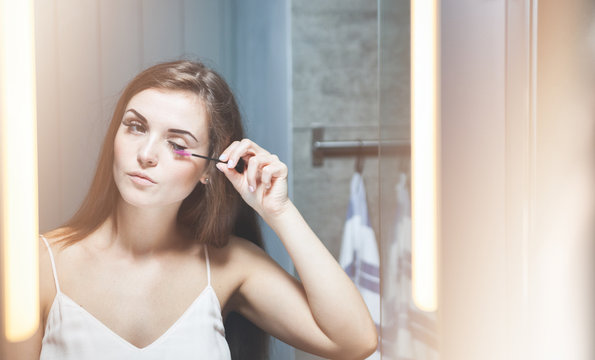 Woman applying mascara on long eyelashes in front of mirror
