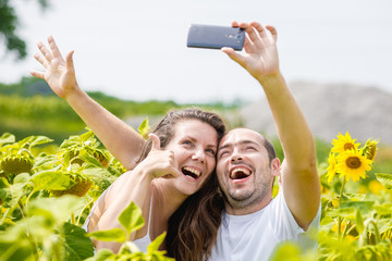 young happy couple man and woman are in a field of sunflowers, make selfie pics