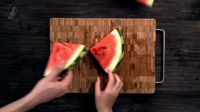 The company of people takes cut pieces of juicy ripe watermelon on black table, flat lay, top view. 4k