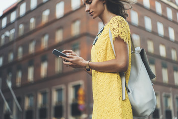 Young hipster girl wearing yellow dress and using modern smartphone outside, attractive smiling...