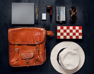 Objects in touristic set ready for a holiday. Leather travel bag, flask, notebook, smoking pipe.