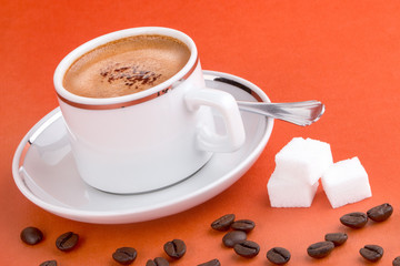 Espresso, Kaffeebohnen und Zuckerwürfel auf orangenem Hintergrund, Makro