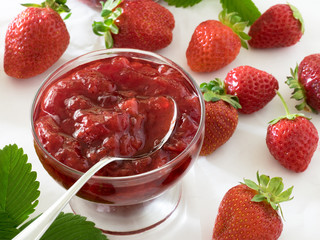 Strawberry jam in a glass bowl, berry and leaf isolated on white background