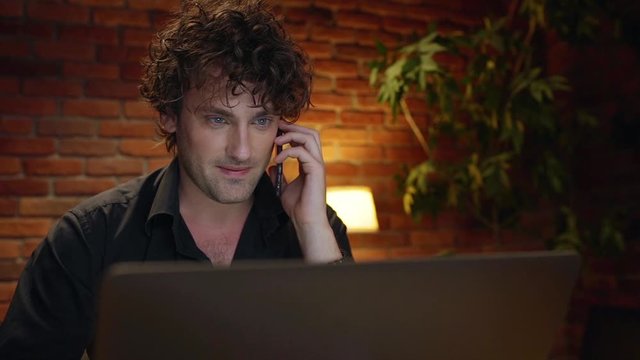 Young successful businessman speaking on phone, smiling, working in office at night. Slow motion.