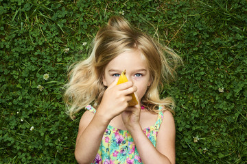 Cute happy little blond girl with melon lying on the grass in summertime