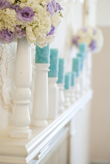 Floral arrangement with white and blue flowers and candles on candle holders. Wedding decor idea. 