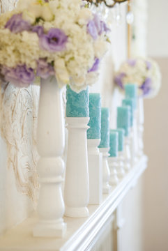 Floral arrangement with white and blue flowers and candles on candle holders. Wedding decor idea. 
