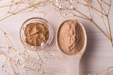 Cosmetic clay powder in a wooden spoon and clay in a jar on a wooden background. Healthy skin care.