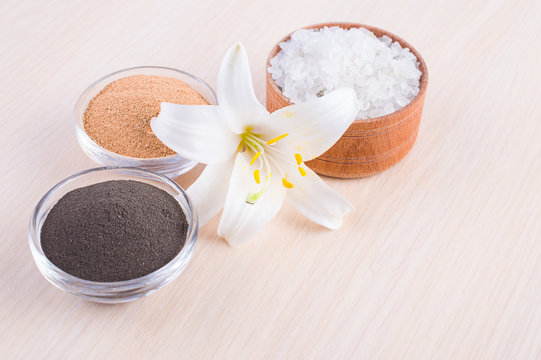Cosmetic clay powder in a jar and a lily flower on a wooden background. Healthy skin care.