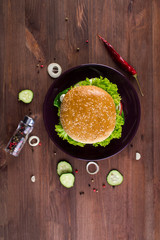Fresh tasty burger with herbs, onions, meat, vegetables and spices on a dark wooden table. Fastfood meal. Flat lay.