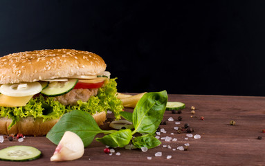Fresh tasty burger with herbs, onions, meat, vegetables on a dark wooden table. Fastfood meal.
