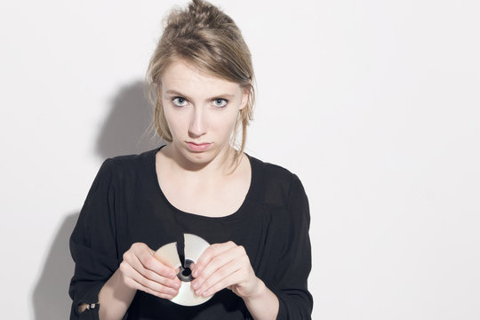 Young blonde woman damaging a compact disc, looking to camera, over a white background.