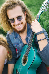 Young curly hippie male with beard and guitar outdoors