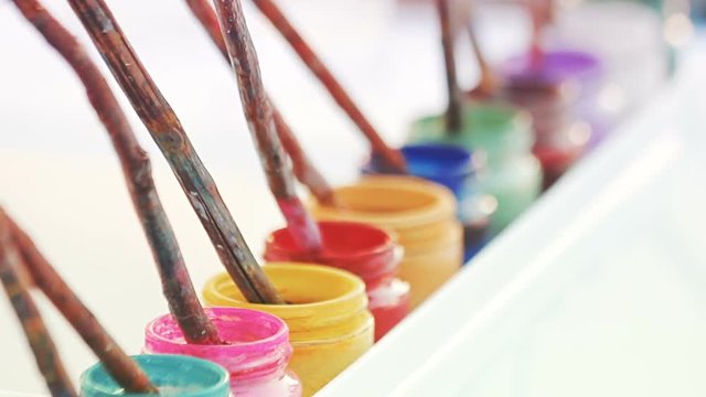 Jars of colorful paint with brushes made out of real branches. Painter's workplace equipment.