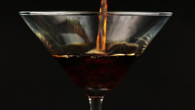 Pouring brown cocktail in martini glass on black background