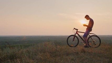 Teenager sitting on the bike uses a smartphone. In the sunset of his silhouette - Powered by Adobe