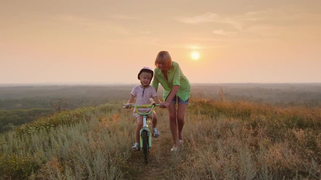Steadicam shot: Mom teaches daughter to ride a bike. Concept - the first success. At sunset