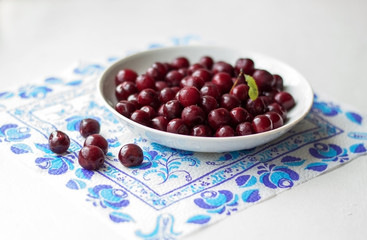 Белое блюдце со спелой вишней стоит на белом подоконнике. Блюдце и салфетка. Вишня на белом блюдце.