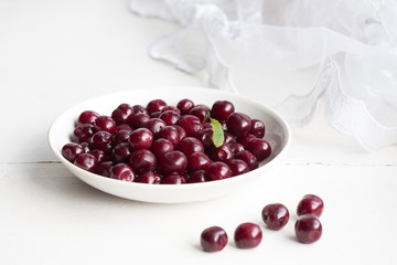 Белое блюдце со спелой вишней стоит на белом подоконнике. Блюдце на подоконнике. Вишня на белом блюдце.