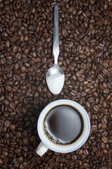 Coffee cup with teaspoon of sugar on coffee beans