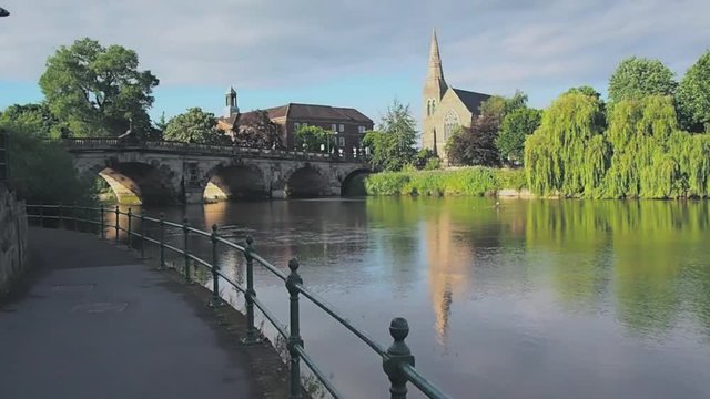 View along the river Severn to the English Bridge, Shrewsbury and a church and prominent willow tree, England, UK.