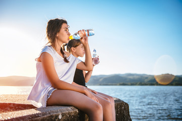 Two girls drinking water and sitting on dock