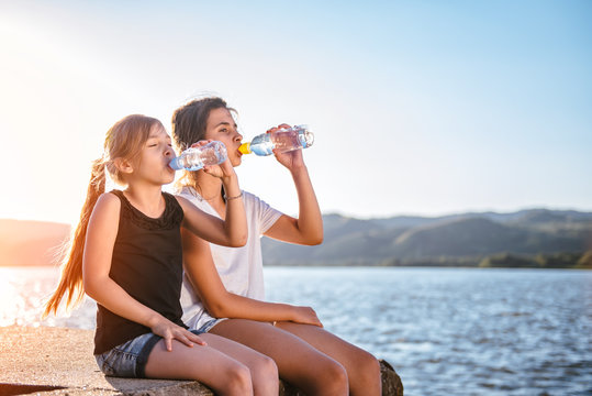Two girls drinking water and sitting by the sea