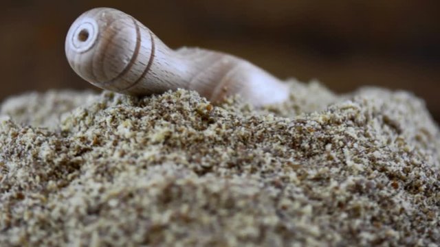 Macro closeup of nutritious ground LSA with wooden scoop rotating on wooden turntable.