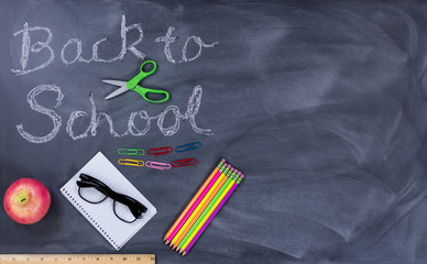 Fototapeta na wymiar Back to school text on erased chalkboard with student supplies