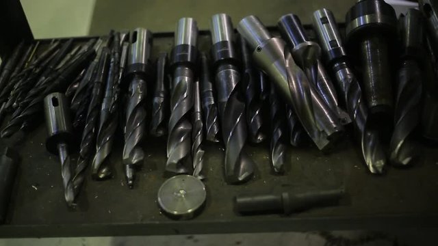 Gear-cutting drill bits for cutting and processing metal parts of machine, lie in a row on shelf.