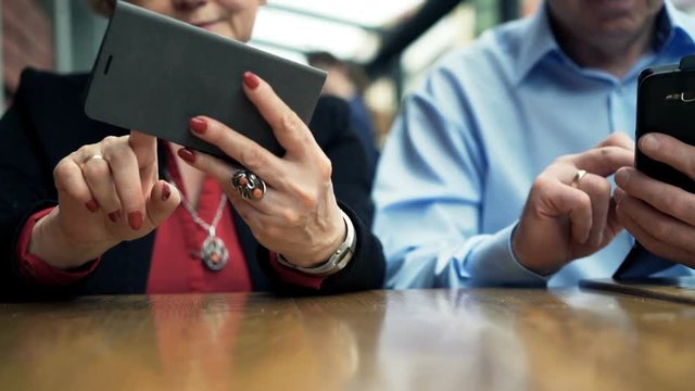 Mature couple hands using smartphone sitting in cafe

