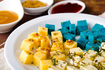 Cheese platter, Gouda, feta, blue pesto cheeses on white plate with herbs, olive oil, pomegranate and mustard sauces